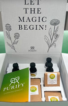A box of Purify Herbs products including various herbal cleanse packages and a green booklet with the text 'LET THE MAGIC BEGIN!' written on the inside cover.