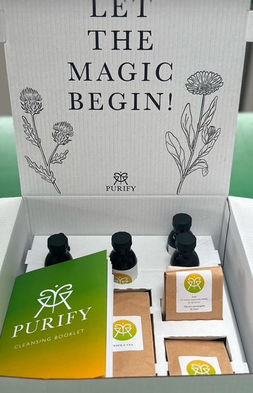 A box of Purify Herbs products including various herbal cleanse packages and a green booklet with the text 'LET THE MAGIC BEGIN!' written on the inside cover.